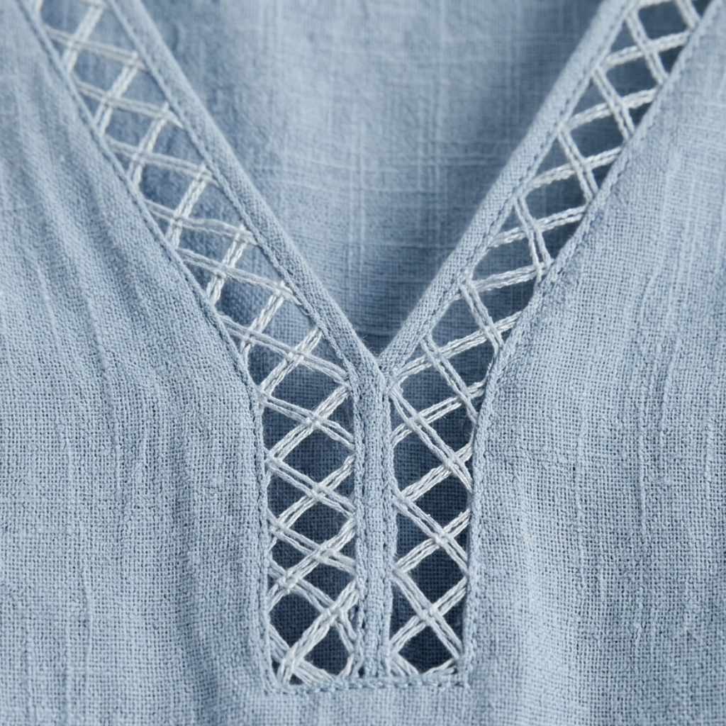 Close-up of a light blue textured fabric garment with a V-neckline and white geometric embroidered trim.